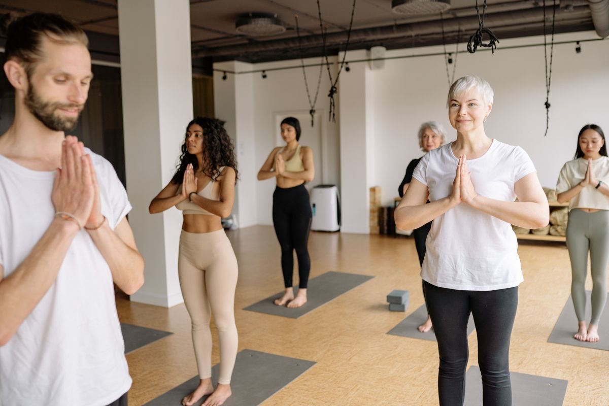 A small yoga class with people of different ages standing with palms together at the chest